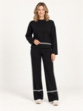 Kendall conjunto negro de suéter y pantalón en modelo rubia sobre fondo minimalista